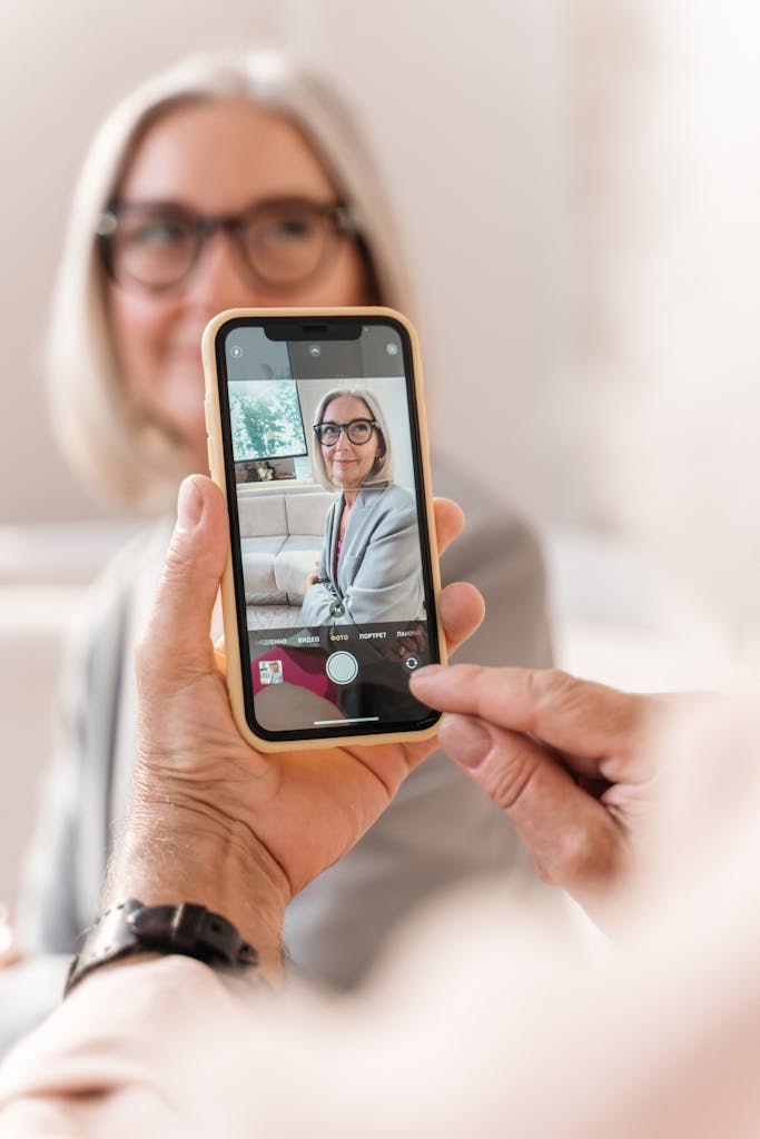 A senior woman taking a selfie with a smartphone indoors, showing her happy expression.